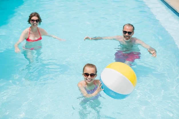 Genitori felici e figlia che giocano con la palla di nuoto in piscina