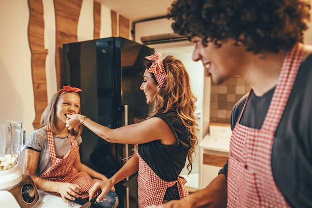 Genitori felici e la loro figlia che cucinano insieme in cucina mentre la bambina li aiuta.