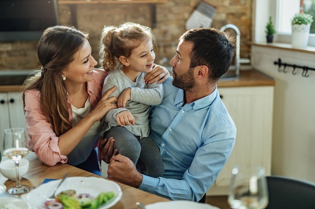 Genitori felici e la loro piccola figlia che parlano dopo un pasto nella sala da pranzo