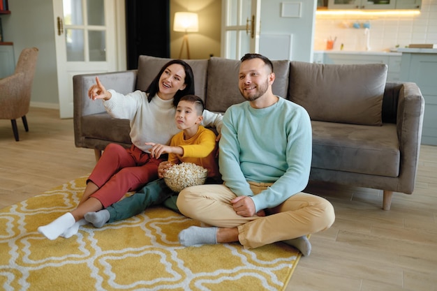 Genitori stupiti e bambini curiosi che guardano il programma televisivo seduti sul pavimento nel soggiorno di casa