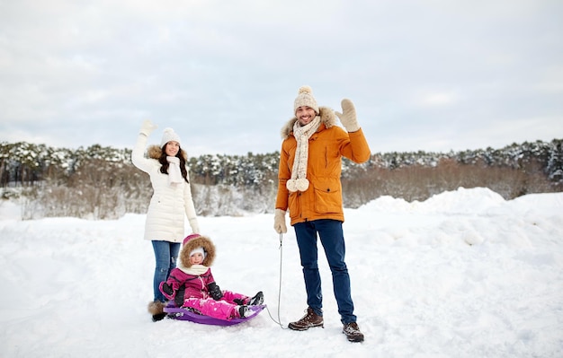 genitorialità, moda, stagione, gesto e concetto di persone - famiglia felice con bambino sulla slitta che cammina e agita la mano in inverno all'aperto