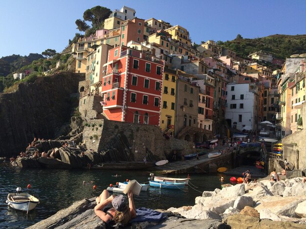 Gente che si diverte sulla riva rocciosa vicino agli edifici contro il cielo