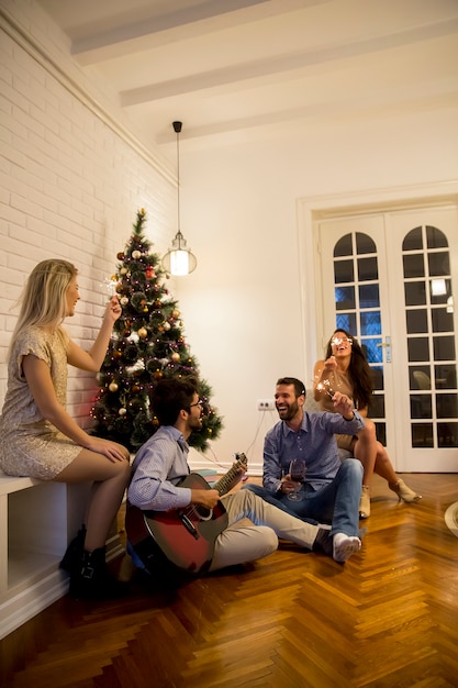 Gente felice che celebra il Natale e il nuovo anno con l&#39;abete a casa e suonando la chitarra