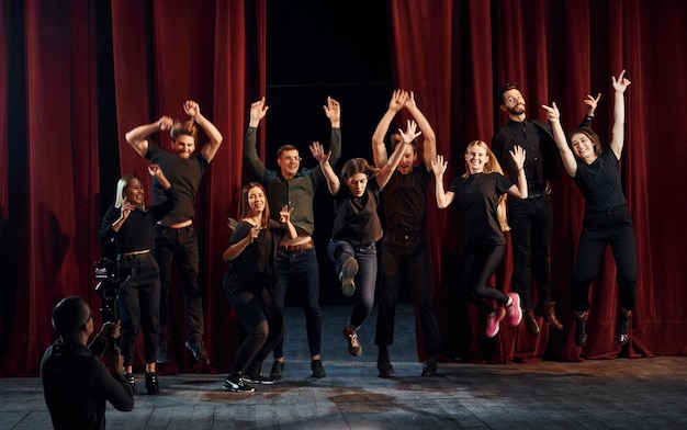 Gente felice che celebra il successo Gruppo di attori in abiti di colore scuro durante le prove a teatro