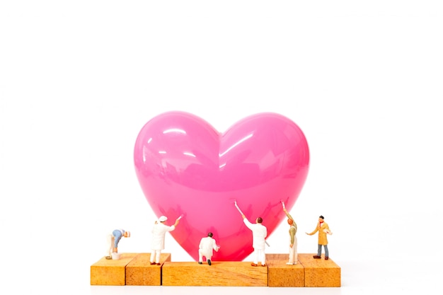 Gente miniatura che dipinge cuore rosa su fondo bianco