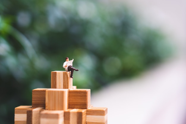 Gente miniatura, uomo che si siede sul collegamento di legno sul fondo verde della natura