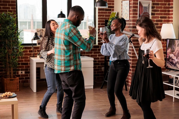 Gente multiculturale, multietnica, felicemente, ballando gioiosamente, bevendo vino, vivendo insieme. Giovani adulti che si divertono ad amici di diverse nazionalità, compagni di festa.