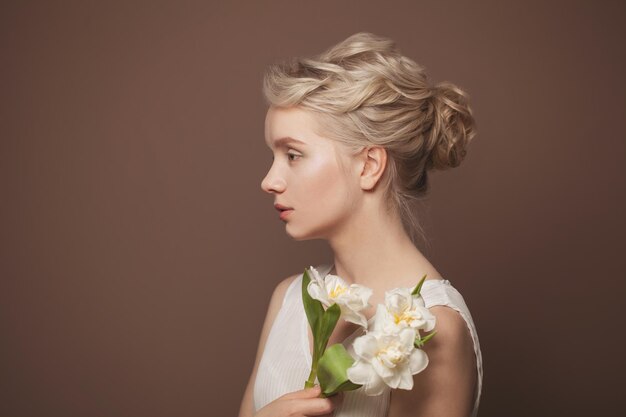 Gentile giovane bellezza giovane donna bionda con fiori bianchi su uno sfondo di bandiera marrone