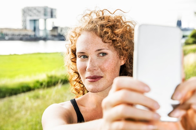 Germania, Colonia, ritratto di giovane donna lentigginosa che si fa selfie con il cellulare