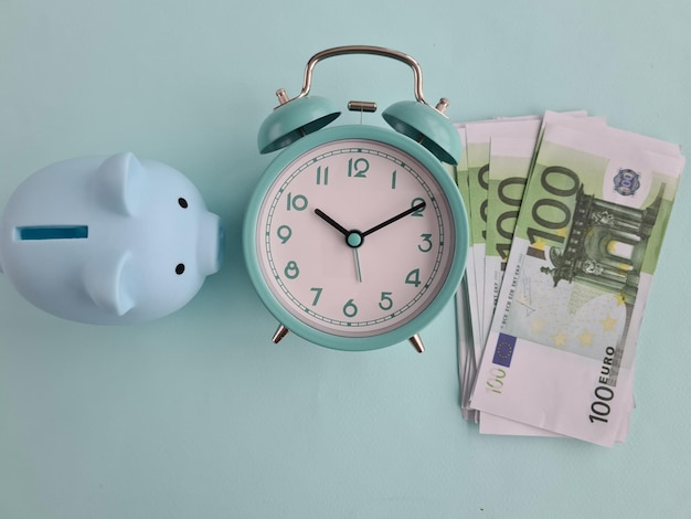 Gestione del tempo e successo finanziario con banconota da 100 euro con sveglia con salvadanaio