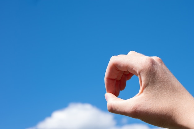 Gesto del primo piano della mano di una donna che fa un anello delle dita isolato su uno sfondo di cielo azzurro con nuvole.