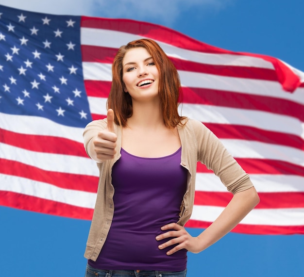 gesto e concetto di persone felici - ragazza sorridente in abiti casual che mostra i pollici in su sullo sfondo della bandiera americana