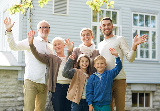 gesto, felicità, generazione, casa e concetto di persone - famiglia felice che agita le mani davanti alla casa all'aperto