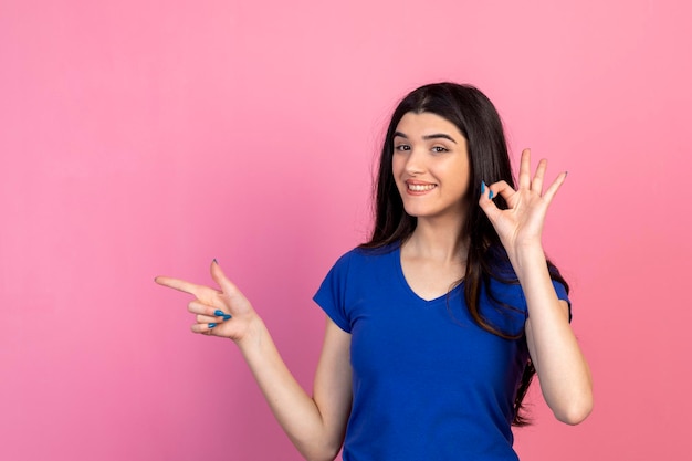 Gesto sorridente della giovane donna Ok e punta il dito da parte Foto di alta qualità