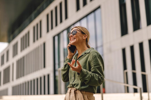 Gestore della donna che parla al telefono con il cliente in piedi sullo sfondo di un edificio moderno