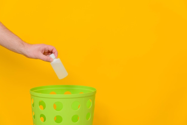 Getta una bottiglia di plastica bianca con del liquido in un bidone della spazzatura verde per lo smaltimento e il riciclaggio