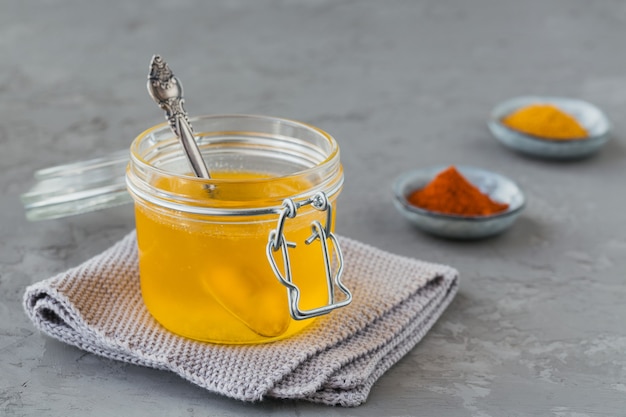 Ghee casalingo sano o burro chiarificato in un barattolo, curcuma e paprika in polvere su cemento grigio