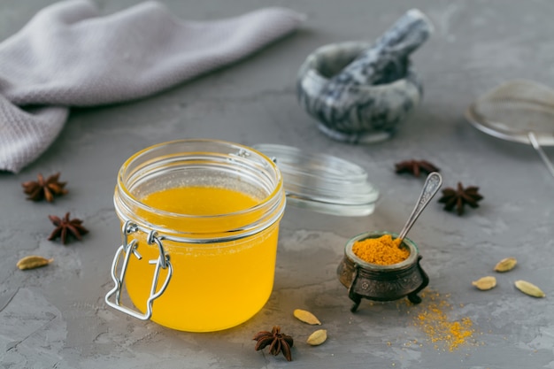 Ghee casalingo sano o burro chiarificato in un barattolo e polvere di curcuma su gray. Un sano concetto di cibo Ayurveda.