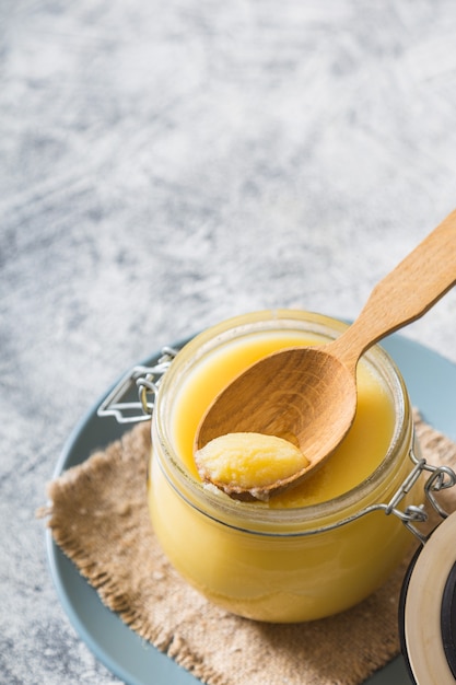 Ghee o burro chiarificato in vaso e cucchiaio di legno sul tavolo grigio. Vista dall'alto. Copyspace. Il burro ghee ha grassi sani ed è un ingrediente di cucina comune in molti piatti della cucina indiana