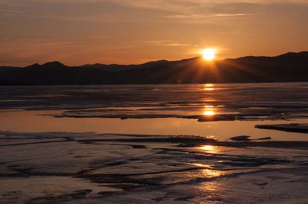 Ghiaccio e acqua vicino alla montagna sul lago Baikal congelato. Tramonto