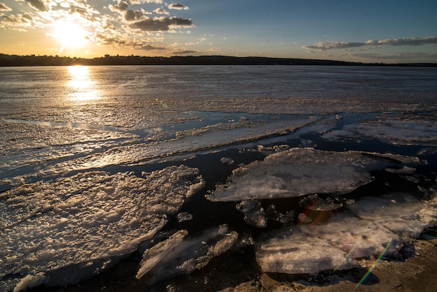 Ghiaccio incrinato intorno alla riva sulla superficie del lago disgelo al tramonto paesaggio invernale grandangolare