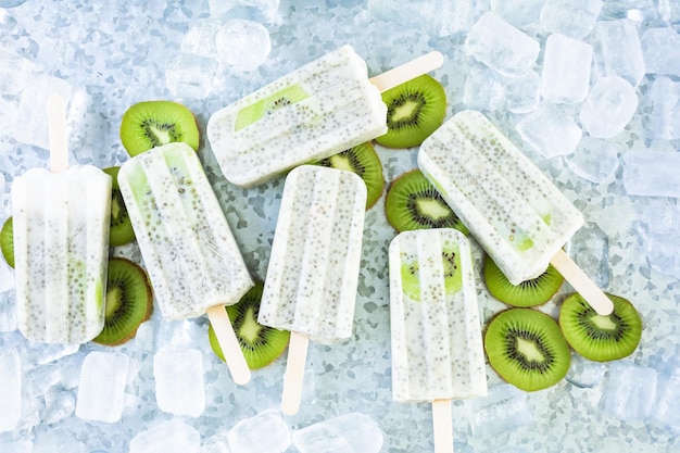 Ghiaccioli di chia di cocco e kiwi con kiwi fresco e ghiaccio nel vassoio di metallo.