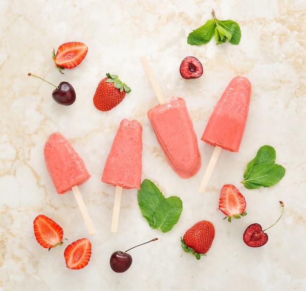 Ghiaccioli di gelato allo yogurt alla fragola con menta e ciliegia sul vassoio di marmo