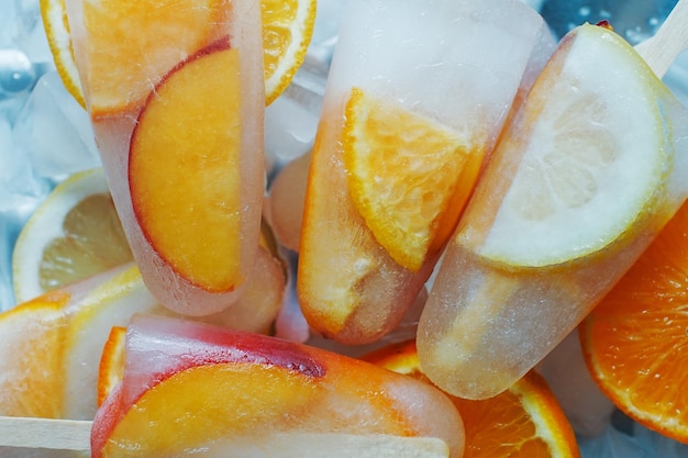 Ghiaccioli fatti in casa all'arancia e alla pesca con fette di ghiaccio e agrumi su sfondo chiaro Concetto di cibo estivo gustoso gelato alla frutta