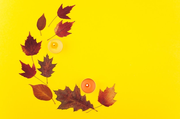 Ghirlanda con acero multicolore e foglie di quercia su sfondo giallo laici piatta. Autunno colorato con candele accese arancioni e rosse