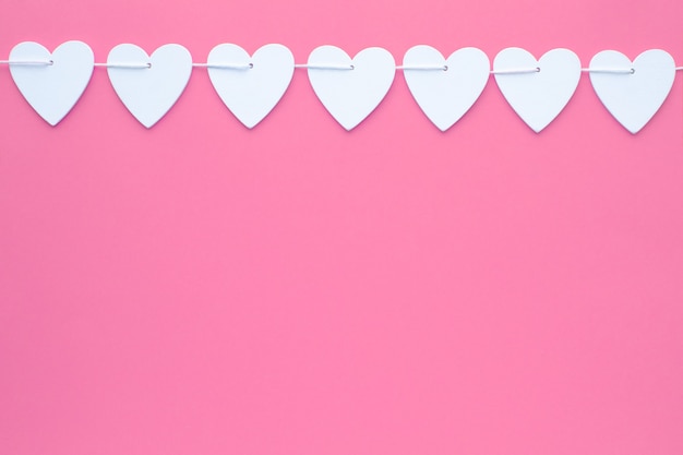 Ghirlanda di cuori in legno bianco in fila su sfondo di carta rosa testurizzata