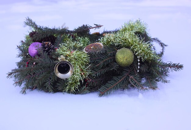 Ghirlanda di Natale decorata con fette d'arancia secche e palline colorate su sfondo bianco di neve.