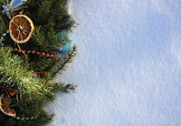 Ghirlanda di Natale decorata con fette d'arancia secche e palline colorate su sfondo bianco di neve.