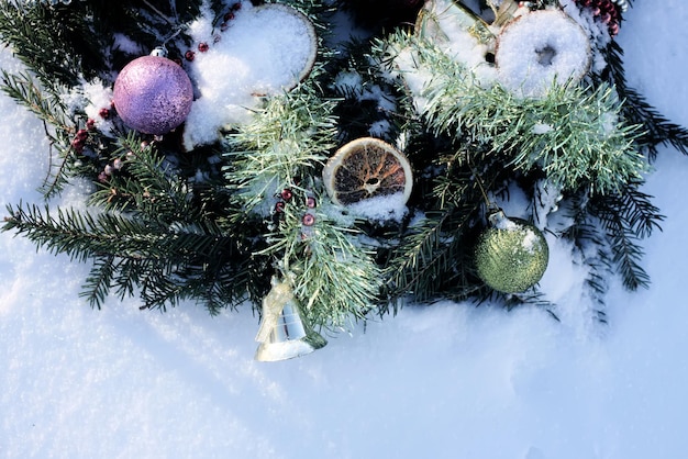 Ghirlanda di Natale decorata con fette d'arancia secche e palline colorate su sfondo bianco di neve.
