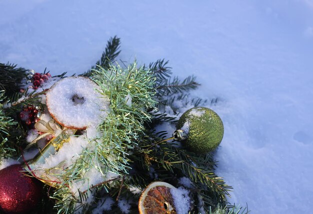 Ghirlanda di Natale decorata con fette d'arancia secche e palline colorate su sfondo bianco di neve.