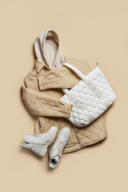 Giacca, felpa bianca con cappuccio e borsa trapuntata e stivali su fondo beige. Felpa alla moda, stile giovanile casual, sport. Abiti eleganti autunnali o primaverili.