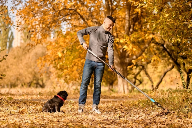 Giardinaggio. Un uomo con rastrello nel parco, il suo cane seduto accanto a lui