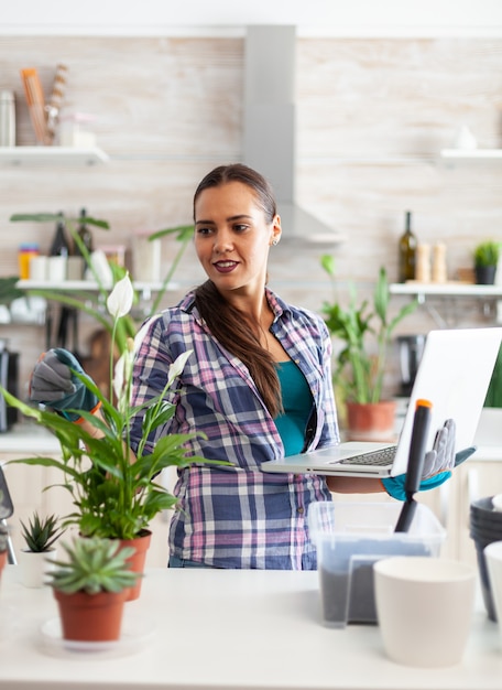 Giardiniere della donna che utilizza il computer portatile in casa mentre decora la cucina con i fiori