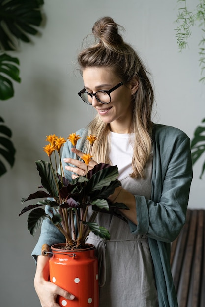 Giardiniere della donna in vestito di lino da portare, che tiene la pianta di calathea in fiore nel barattolo di latte rosso