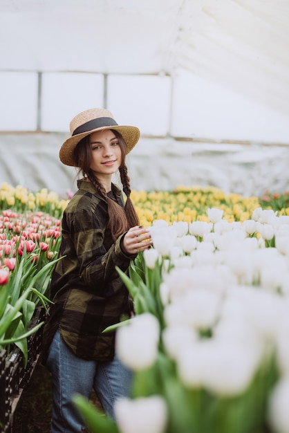 Giardiniere della giovane donna che si prende cura dei fiori dei tulipani coltivati in una serra.