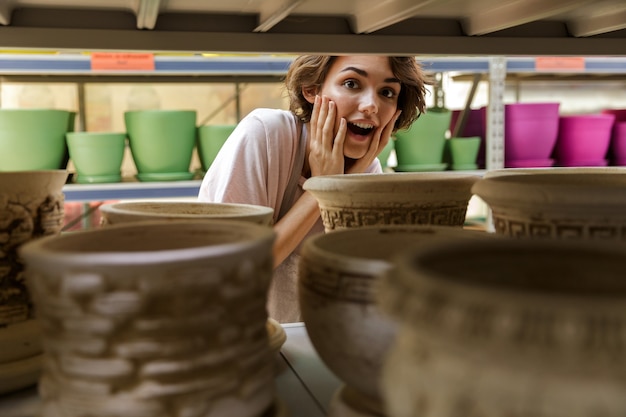 giardiniere donna carina scioccato in piedi in serra scegliendo vaso vaso per piante.