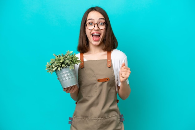 Giardiniere Donna ucraina che tiene una pianta isolata su sfondo blu che celebra una vittoria in posizione di vincitore