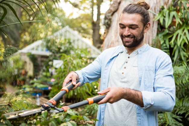 Giardiniere felice che usando i tagliasiepi al giardino