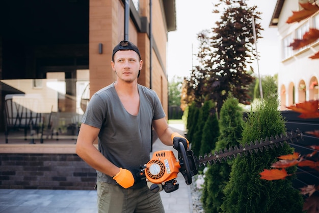 Giardiniere professionista di trent'anni che taglia arbusti verdi attrezzature professionali per pareti in un giardino