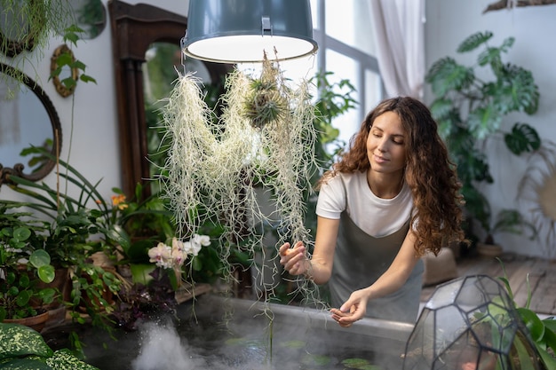 Giardiniere ragazza che si prende cura della pianta acquatica in serra tenendo la pianta d'appartamento sotto il bagno con acqua