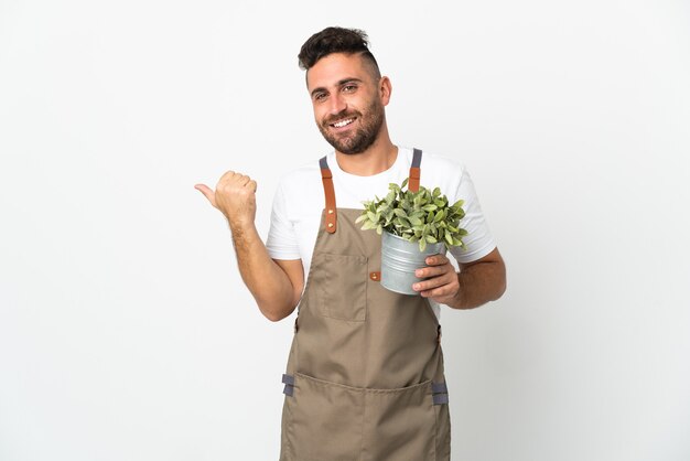 Giardiniere uomo che tiene una pianta su sfondo bianco isolato che punta al lato per presentare un prodotto