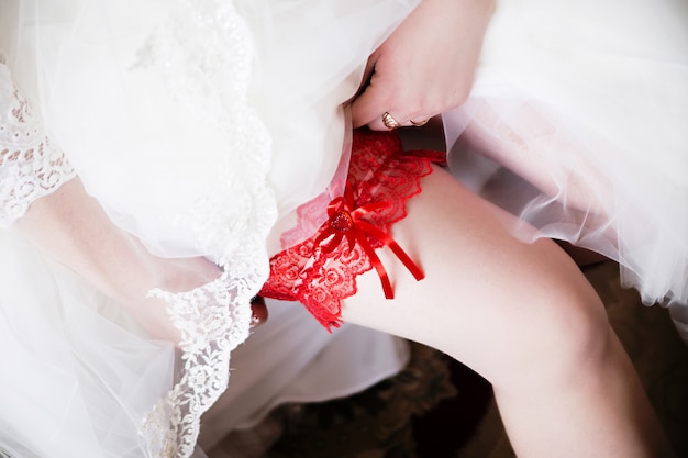 Giarrettiera rossa sulla gamba della sposa, sposa del mattino, la sposa indossa una giarrettiera sulla gamba