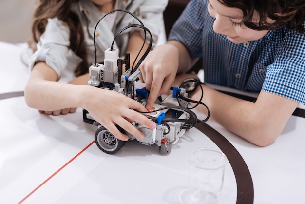 Gifted young generation. Clever skilled involved children sitting in the laboratory and creating robot while studying