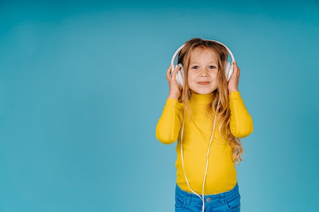 Gilr carino bambino piccolo ascolta musica su grandi cuffie bianche isolate su sfondo blu