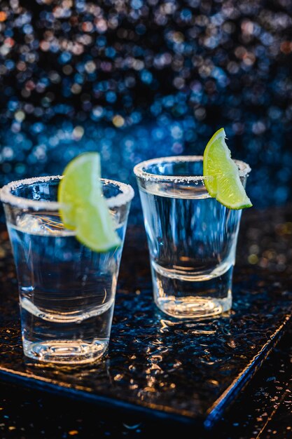 Gin o vodka con lime. Due bicchieri con un cocktail alcolico con limoni sulla superficie blu nera. Vodka, cocktail, alcolici, bevande, ristorante, concetto di relax.