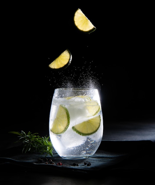 Gin tonic con pezzi di limone in un fondo scuro di vetro